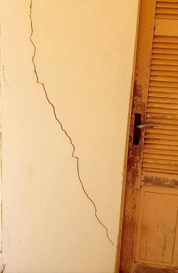 Une grande fissure court le long d'un mur jaune à côté d'une porte en bois usée à la peinture écaillée.