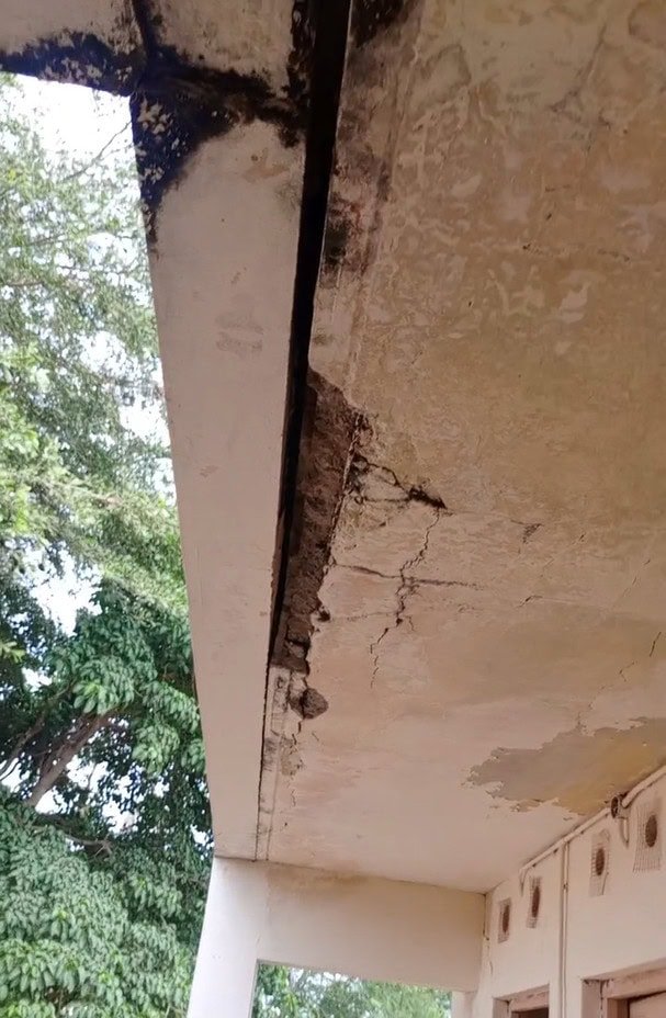 Toit en béton fissuré et endommagé avec des trous visibles et des taches d'eau près de l'extérieur d'un bâtiment.