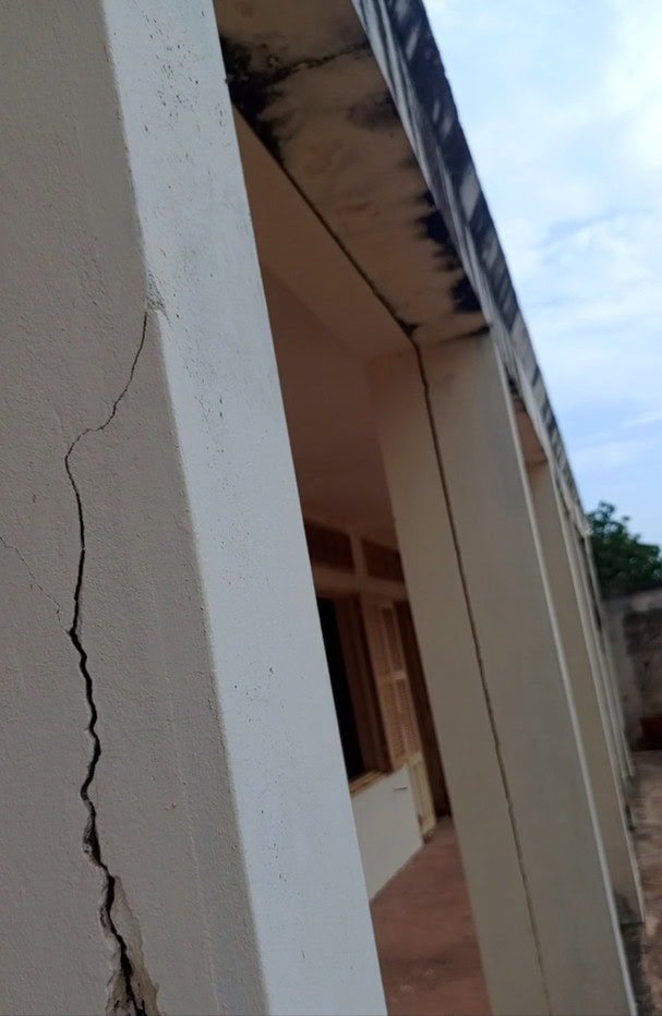 Colonne de bâtiment présentant une grande fissure verticale et des taches de moisissure noire près du toit.