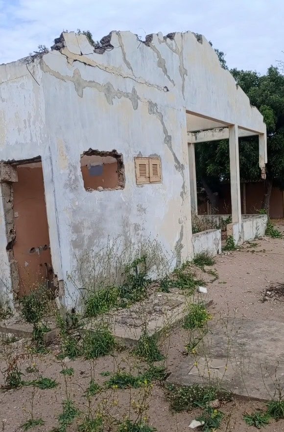 Un bâtiment partiellement effondré, usé par les intempéries, dont la peinture s'écaille et qui est entouré de mauvaises herbes.